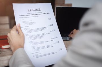 Person's left hand holding a resume with their right hand touching a laptop keyboard
