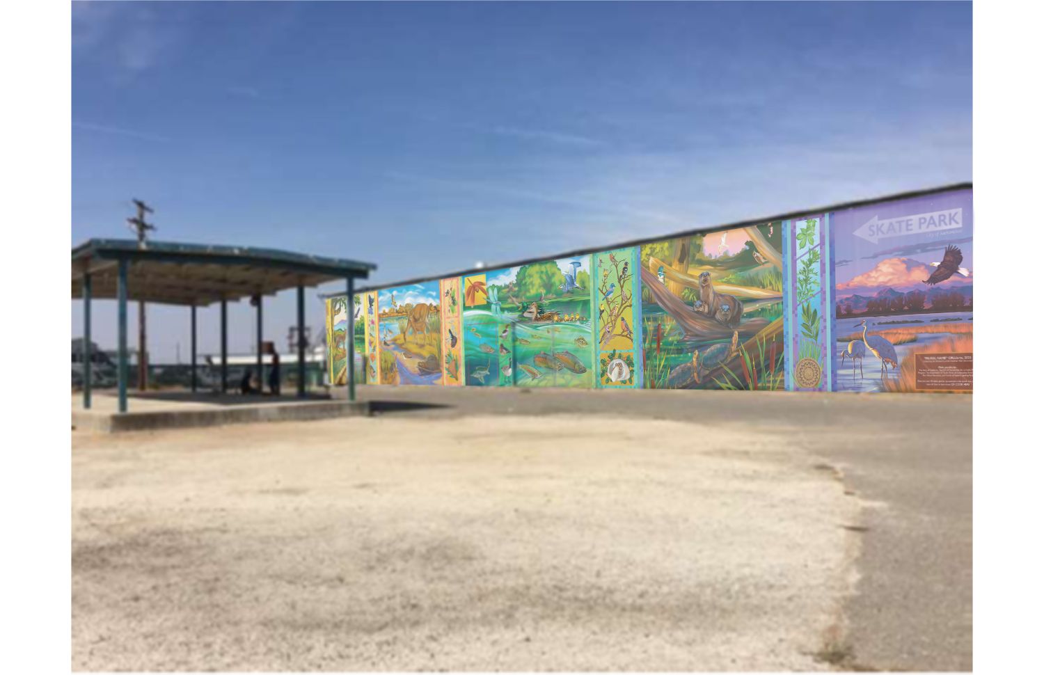 Mural photoshopped onto building next to a shade structure against blue sky with a dirt road in the foreground.