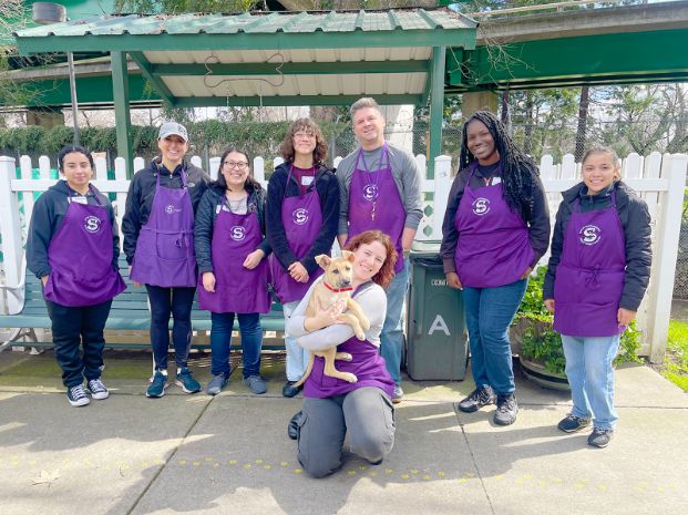 group of volunteers wearing a purple apron and standing in front of a white fence
