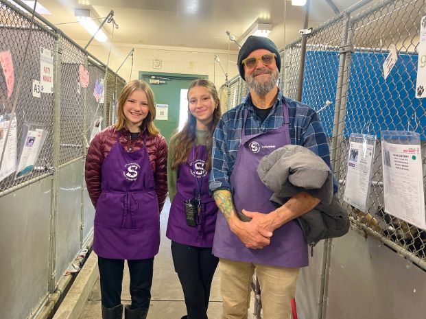 Teen volunteers and adult supervisor wearing a purple apron and standing inside the dog kennel building