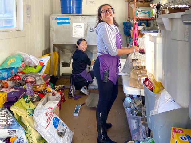 two youth volunteers working inside a storage building and putting pet food into bags