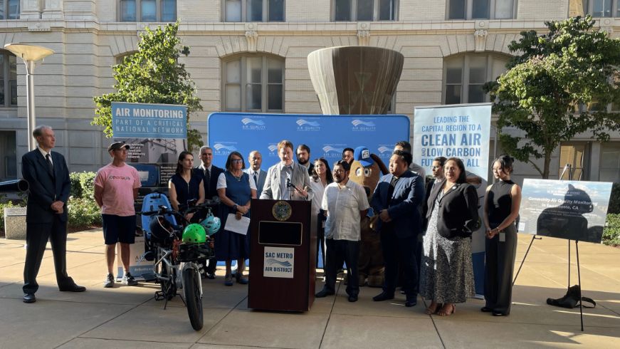 Group of people in front of podium. Sign that says Clean Air Day in the background.