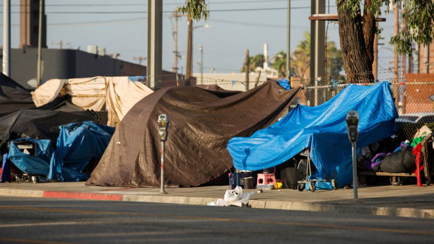 Tents on sidewalk, parking meters, trees, street