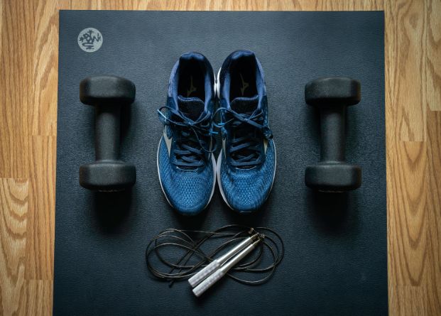 exercise mat with tennis shoes, weights, and a jump rope laid out on top