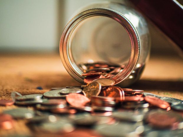 tipped over glass jar with coins falling out of it on table