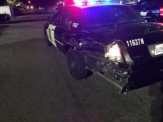 A photo of a fully marked police vehicle damaged by the suspect's vehicle. Panels from the driver's side of the parked police vehicle were torn off in the crash..
