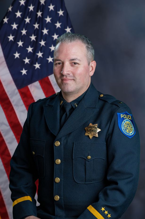 Photo of Chad Coughran in uniform standing in front of the American flag.